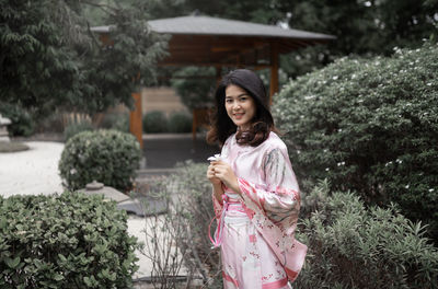 Portrait of smiling young woman standing against trees