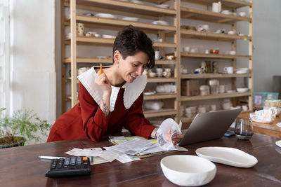Satisfied successful female ceramic studio owner calculating revenue, doing bookkeeping