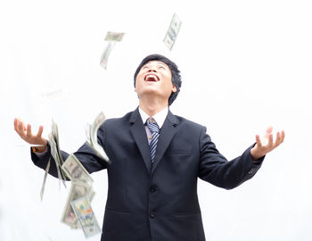 Paper currency falling on cheerful businessman standing against white background