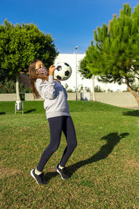 Full length of woman in mask playing with soccer ball at lawn