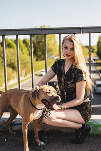 Portrait of young woman sitting by dog on footbridge