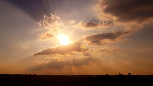 Sunlight streaming on silhouette landscape against sky during sunset