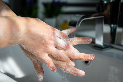 Close-up of hand touching water from faucet at home