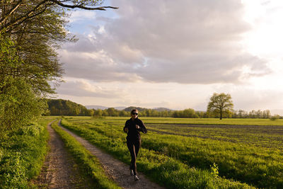 Mid adult woman jogging on land against sky during sunset