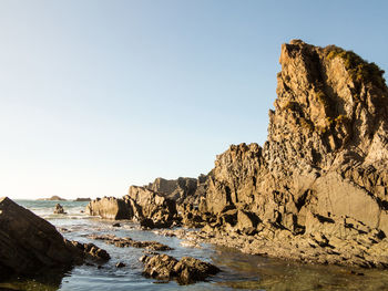 Rock formations by sea against clear sky