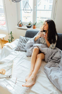 High angle view of thoughtful young woman looking away while having coffee on bed at home