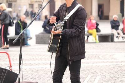 Midsection of man playing guitar while standing on street in city