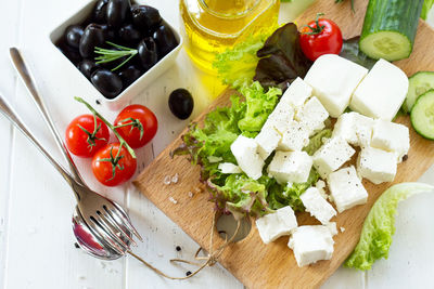 Cooking qreek salad with fresh vegetables, feta cheese and black olives on a white wooden table.