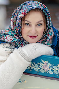 A slavic woman in a national colored scarf, a fur coat and  mittens on the porch of a wooden house