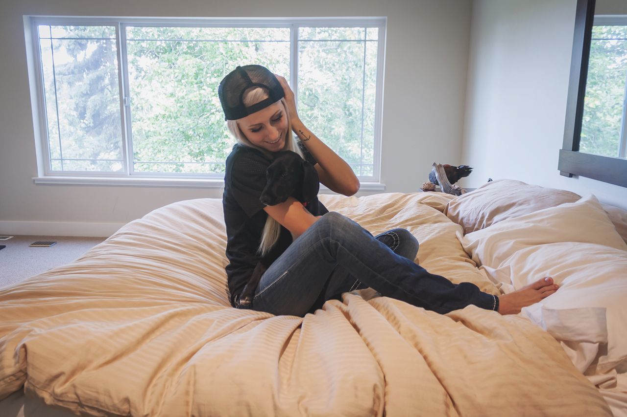 BEAUTIFUL YOUNG WOMAN SITTING ON BED AT HOME