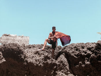 Portrait of man in sunglasses standing on rock against clear sky