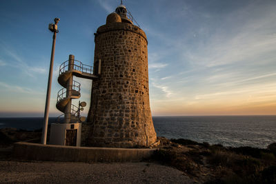 Lighthouse by sea against sky during sunset