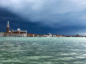 View of buildings by sea against cloudy sky