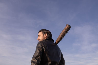 Mid adult man with barbed wire wrapped baseball bat looking away against sky