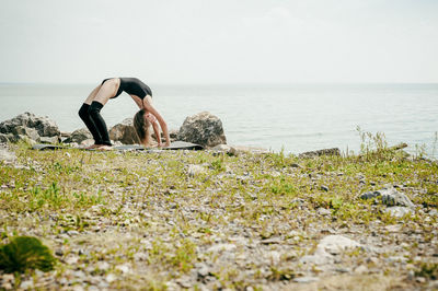 Young woman doing yoga at beach against sky