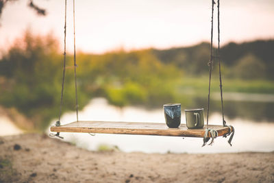 Close-up of swing next to lake with coffe mugs