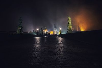 Illuminated buildings by street against sky at night