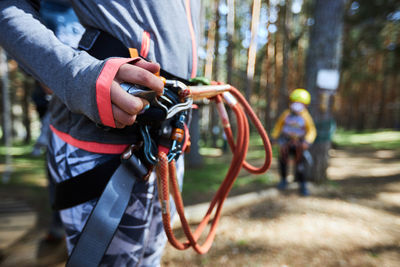 Soft focus of anonymous kid adjusting safety ropes attached to belt on waist while spending weekend day in adventure park in forest