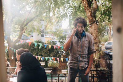 Young man talking on mobile phone while standing in balcony during party