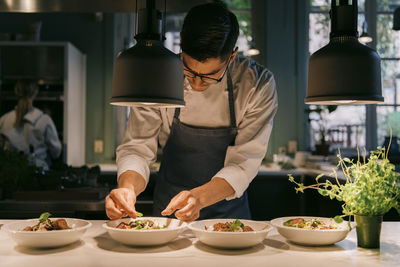 Male chef garnishing food with herb under light at commercial kitchen