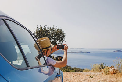 Man taking picture with smarphone from open window of a car stopped roadside with a beautiful view 