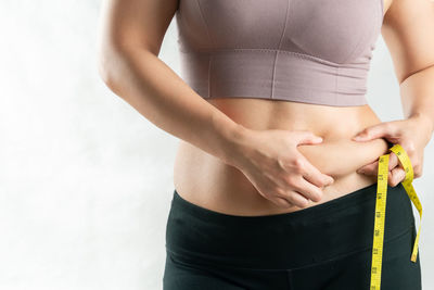 Midsection of woman holding hands standing against white background