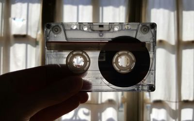 Cropped hand of person holding audio cassette against window