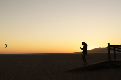 Silhouette man standing on beach against sky during sunset