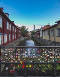 Love locks on railing over canal in city against sky