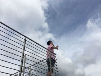 Low angle view of carefree man standing on balcony against cloudy sky