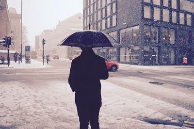 Rear view of man standing on city street during snow fall