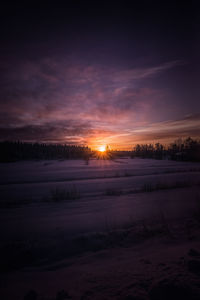 Snowy field against sky during sunset