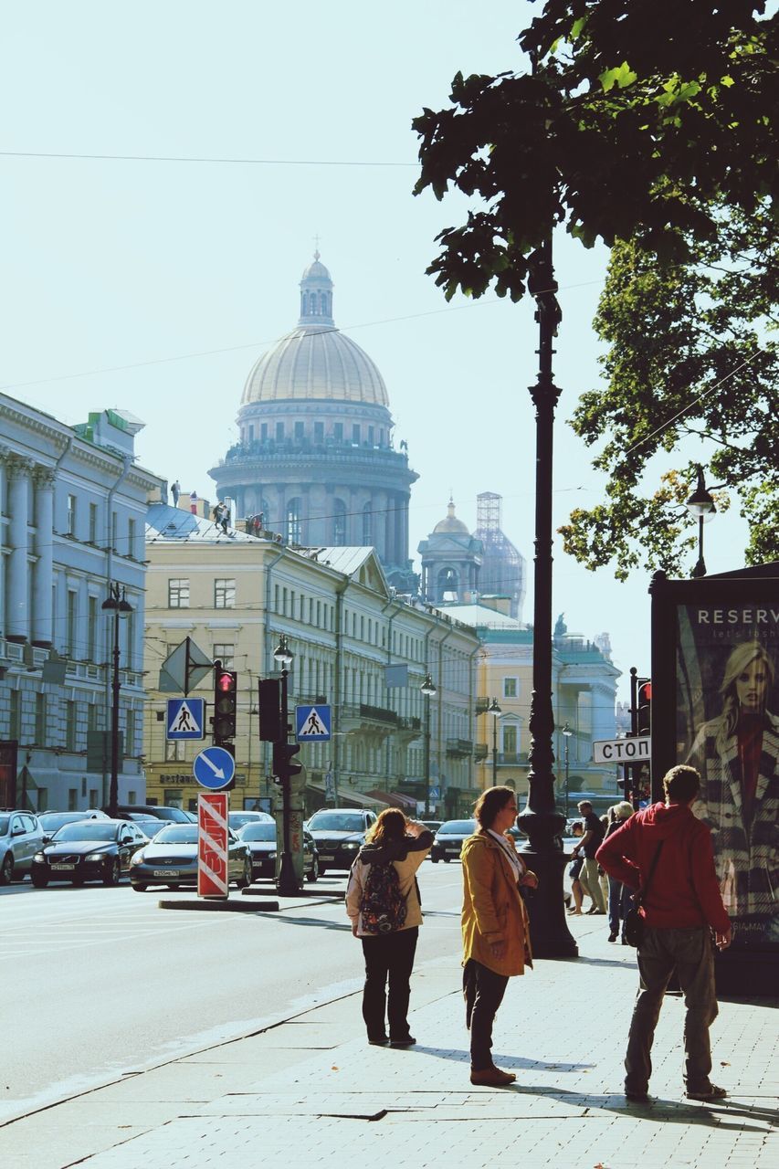 building exterior, architecture, built structure, city, walking, street, men, person, city life, rear view, lifestyles, city street, large group of people, road, full length, clear sky, travel, leisure activity, transportation