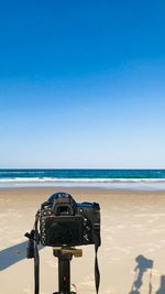 Camera on beach against clear blue sky