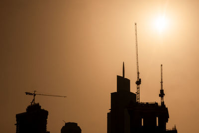 Low angle view of cranes at construction site during sunset