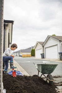 Young boy shoveling dirt into wheelbarrow in back alley