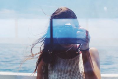 Close-up portrait of woman holding smart phone against sky