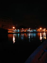 Illuminated city by river against sky at night