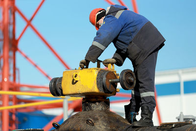 A worker in overalls and a hard hat repairs and maintains a linear crane of the main gas pipeline 