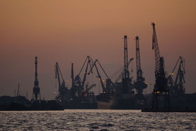 Cranes at commercial dock against clear sky during sunset