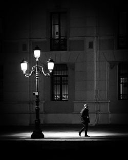 Full length of man walking on illuminated street against building at night