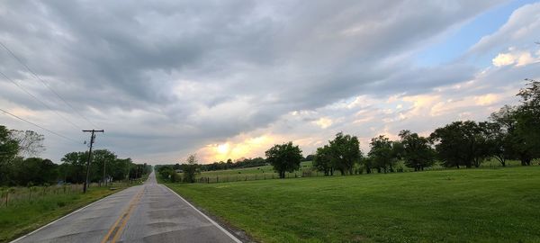 Road by trees against sky during sunset