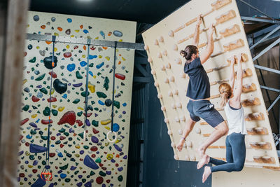 Full body side view of anonymous barefoot sportspeople in activewear practicing climbing on wall with wooden grips in light gym