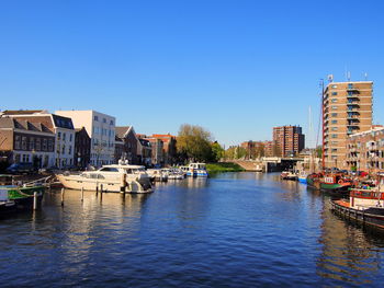 Sailboats moored in canal by buildings against clear blue sky