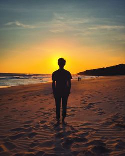 Silhouette man standing on beach against sky during sunset