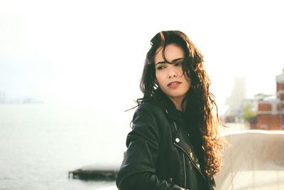 Thoughtful young woman standing at balcony by sea against clear sky