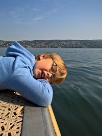 Close-up portrait of young woman lying on shore against sea