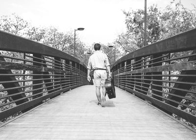 Rear view of man carrying guitar case on footbridge