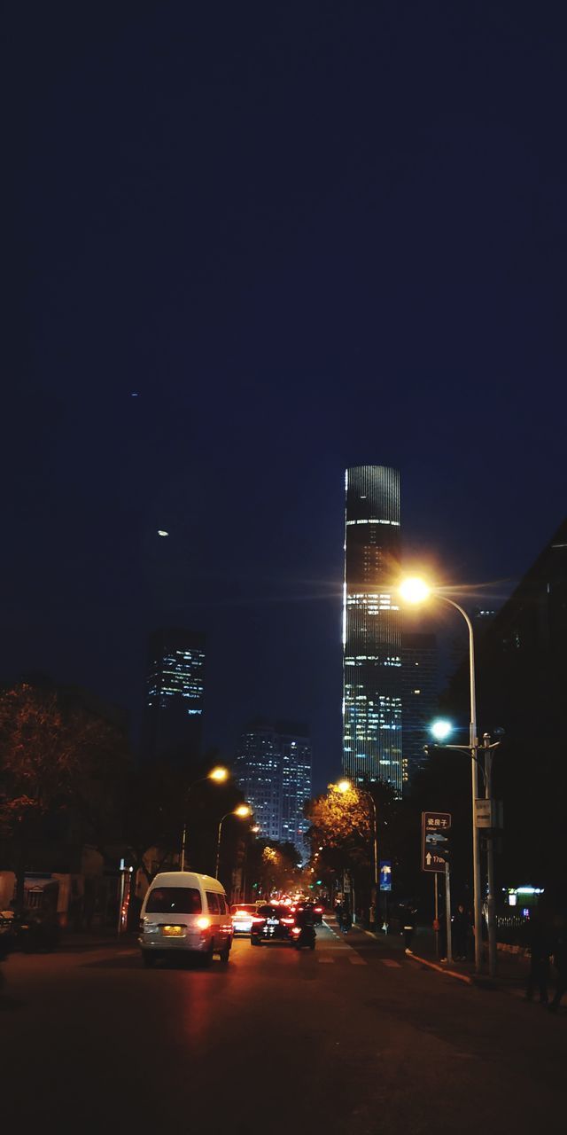 ILLUMINATED STREET BY BUILDINGS AGAINST SKY AT NIGHT