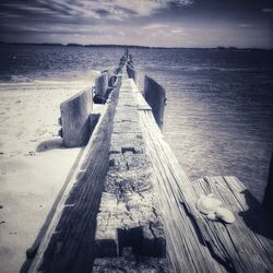 Wooden jetty leading towards sea against sky